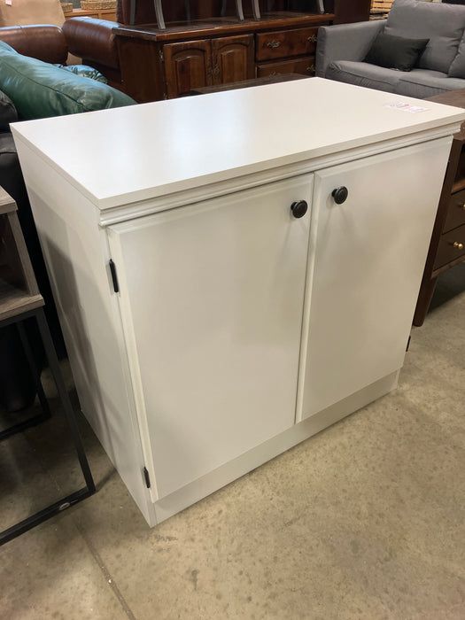 White cabinet with black knobs on a concrete floor