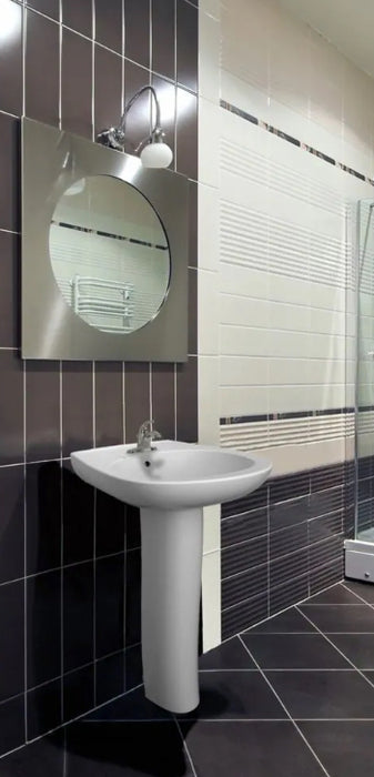 Bathroom with a white pedestal sink against a tiled wall.