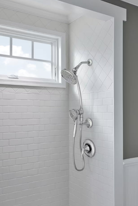 Shower head and control handle mounted on a tiled shower wall with a window in the background.