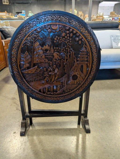 Decorative wooden table with intricate carvings on a stand in a store setting.